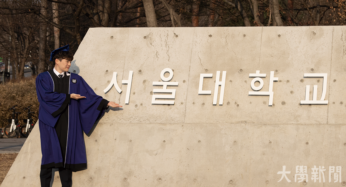 한 졸업생이 새롭게 설치된 한국어 교명 조형물 앞에서 포즈를 취하고 있다.